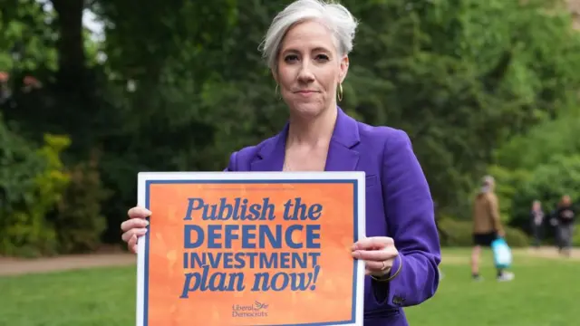 Daisy Cooper holding a sign which says 'publish the defence investment plan now!'