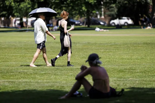 A man walks alongside a woman with an umbrella to shelter from the heat at London Fields
