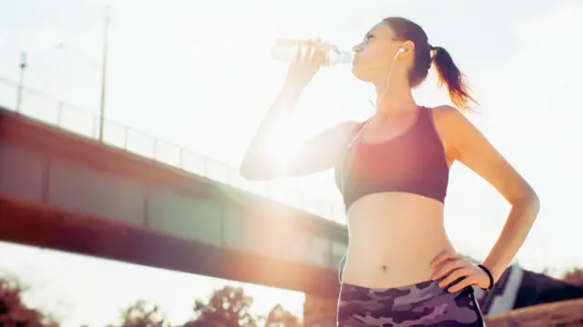 Woman in running gear drinking from water bottle