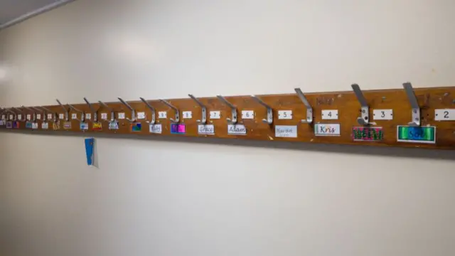 A row of empty coat pegs at a school, with small handwritten nametags below them.