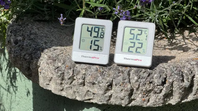 Indoor thermometers sat on a rocky shelf displaying temperatures of 49.8C and 52.1 C