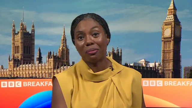 Kemi Badenoch, a woman, sitting in front of a TV set showing Big Ben and the straps "BBC Breakfast" written in white against an orange background.