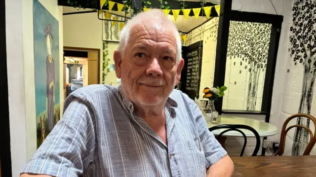 A man in a striped shirt sat at a kitchen table.