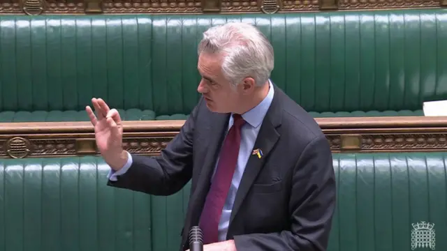 James Cartlidge speaking in the House of Commons, wearing a suit and tie and gesturing with his right hand.