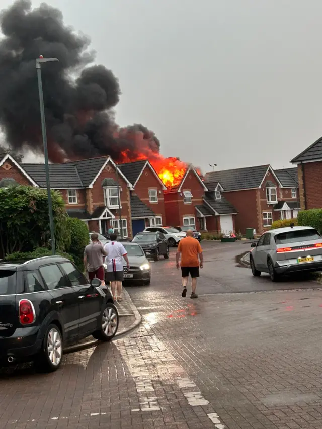 Fire in roof of home, with people and cars in front