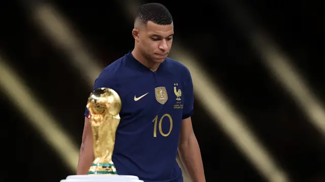Kylian Mbappe walks past the World Cup trophy in 2022