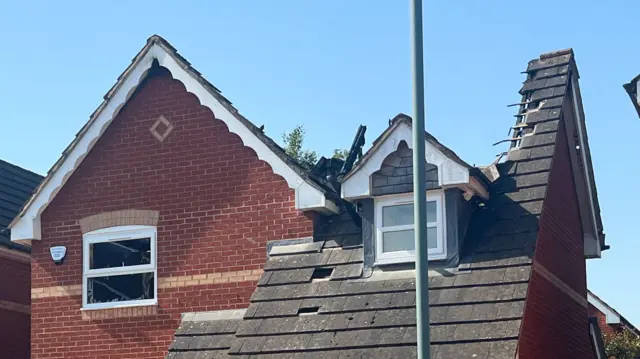 A closer shot of the burnt out roof of a red-brick detached home.