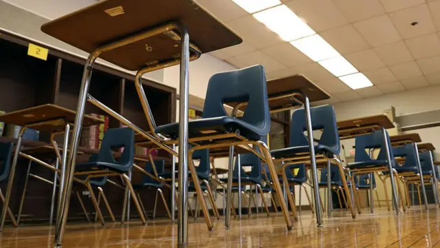 A picture showing several rows of blue plastic chairs and wooden desks inside a classroom, taken from down on the floor looking upwards.