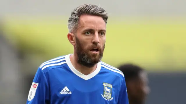 A footballer player during a match. He is wearing a blue football shirt. He has short dark hair with some grey in it.