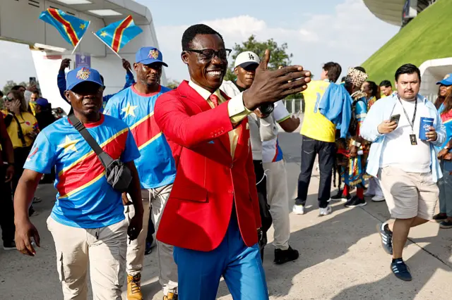 Michel Kuka Mboladinga wearing a red suit jacket and blue trousers