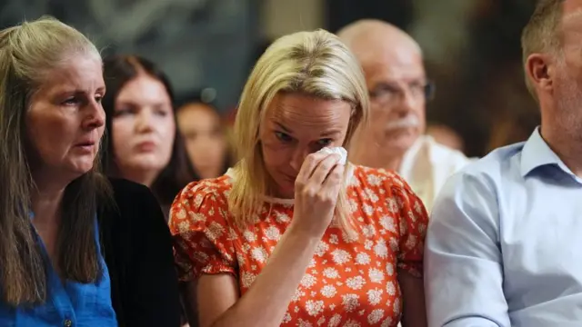 A woman wipes tears from her eyes while sitting between a man and a woman.