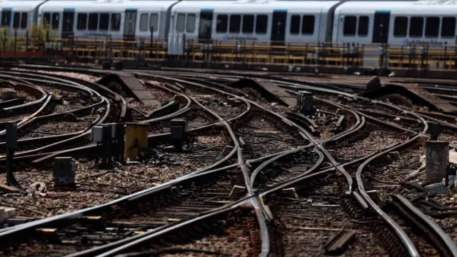 Railway tracks at Waterloo Station in London. A train can be seen in the background, with intersecting lines visible in the foreground.