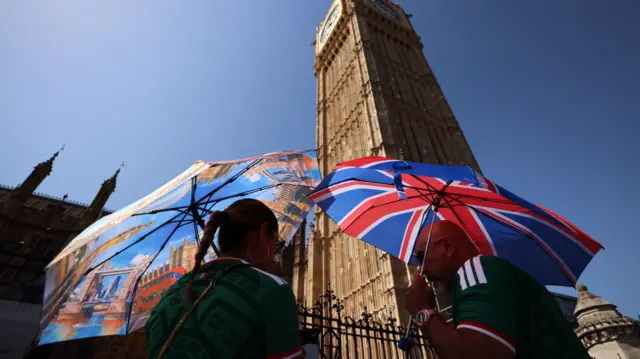 Pedestrians shelter from the sun while passing parliament in London, on 24 June 2026.