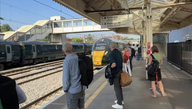 People stand at train platform while train approaches