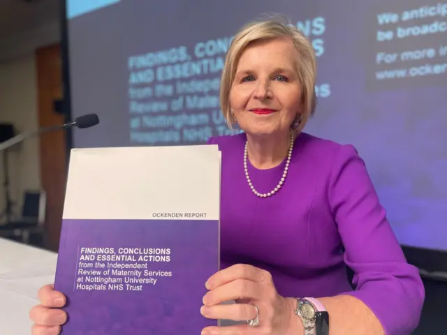 Donna Ockenden, wearing purple, holds up a copy of her report