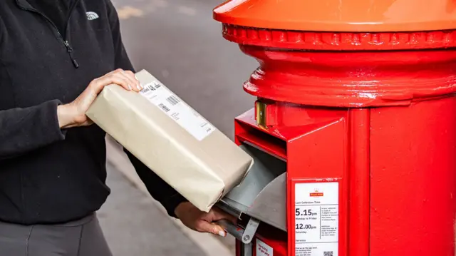 A brown parcel being posted in a red post box.