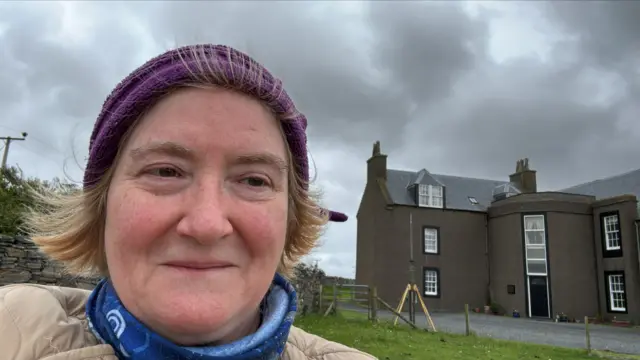 Woman wearing beanie hat taking a selfie as she stands outside building