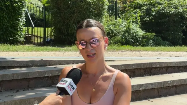 A woman wearing sunglasses, speaking into a BBC News branded microphone.