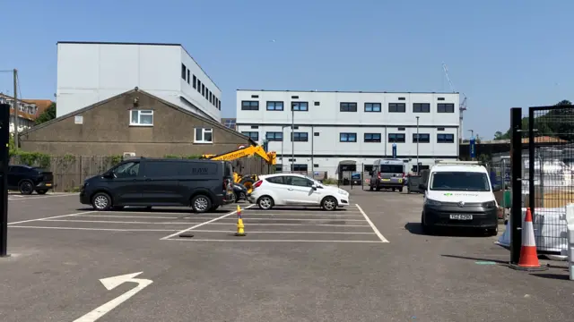 A school building, which is made up of two modern blocks which are square and light blue, pictured behind a car park.