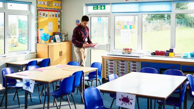 A male teacher in an empty school classroom