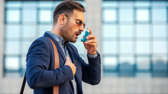 Young businessman treating asthma attack with inhaler