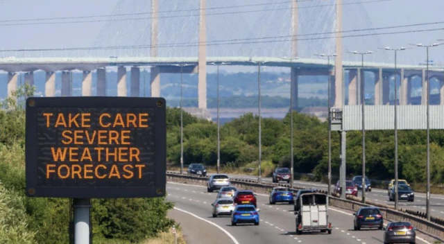 A motorway sign in front of the Prince of Wales Bridge reads 'Take Care Severe Weather forecast'. It is a sunny day.