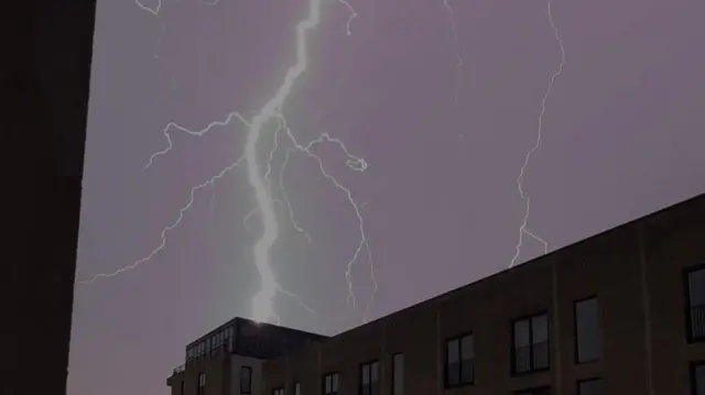 A large fork of lightning with many smaller forks branching off of it strikes a large building.