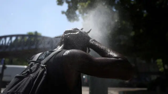 A man washes his face and hair to stay cool in a city centre fountain.
