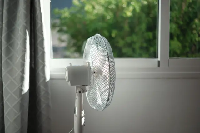 A white fan in a room with grey curtains and white walls.
