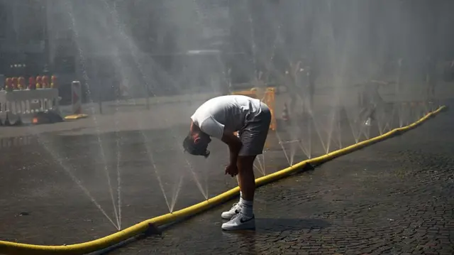 A man cools his head at water hoses spilling water to provide relief from the summer heat in Cologne, Germany