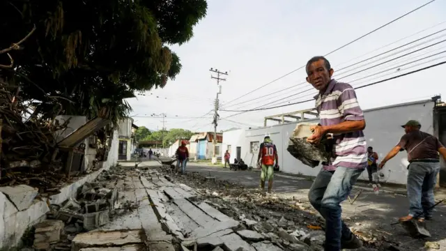 A man carries a large bit of rubble away from a damaged house