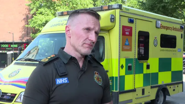 A photo of Jason Killens, wearing an NHS ambulance uniform and stood outside in front of an ambulance