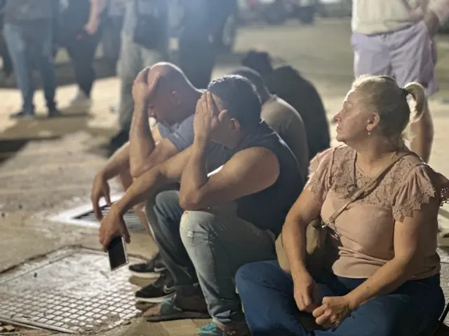 Three people sat down on the street, two with their heads in their hands