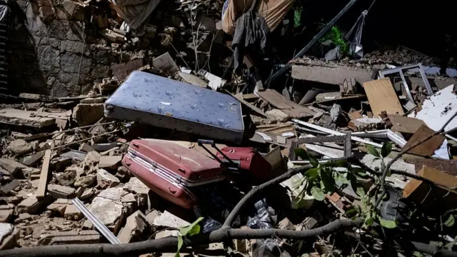 Suitcases seen among rubble, which includes bricks and a branch in a harshly lit photograph