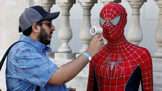 A man holds a fan up to someone dressed in a spiderman costume
