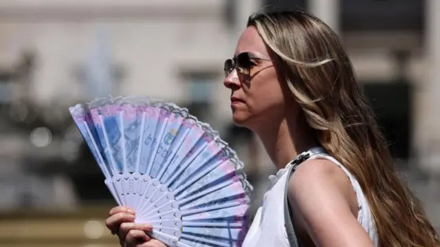 A woman uses a fan to cool down in London, 24 June 2026