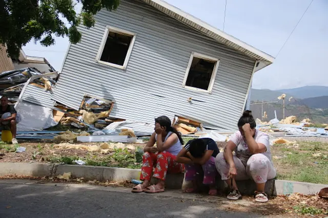 Three people put their heads in their hands as they sit outside a damaged home in Caracas
