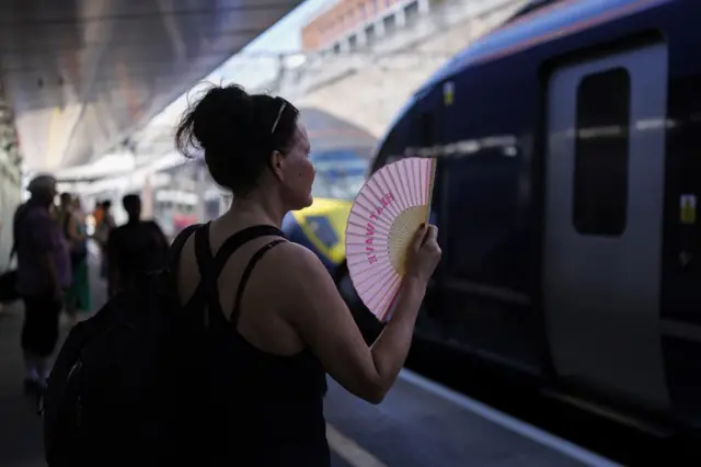 A passenger uses a fan to cool down on a train platform