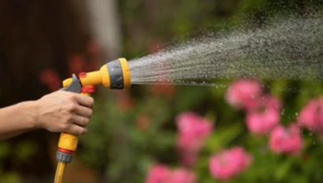 A person holding a yellow hose and spraying water.