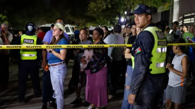 People wait outside their homes in Caracas while law enforcement officers watch on