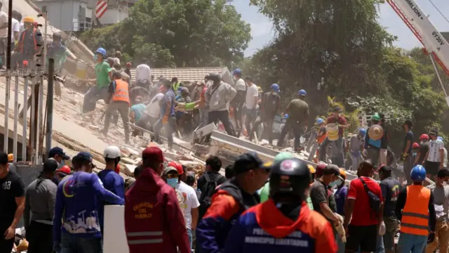 Dozens of emergency workers, some wearing hard hats and masks, search through the rubble of a collapsed building