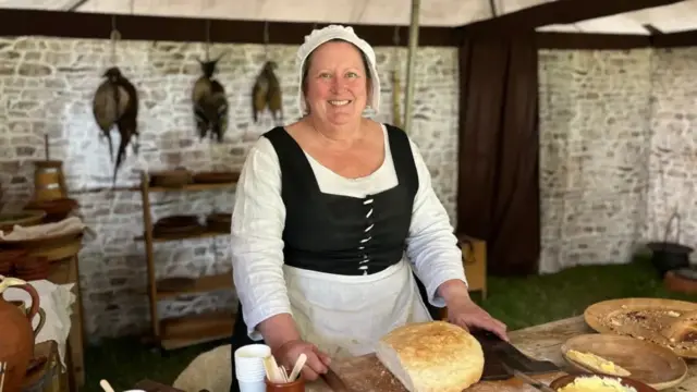 Woman in Tudor white hat stood in front of freshly made bread while standing in a kitchen