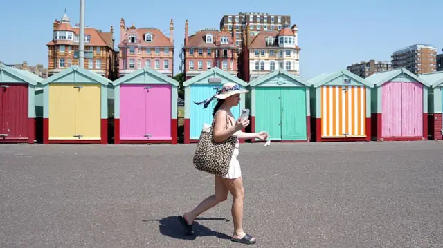A person walks in the sun past beach huts.