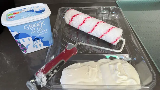 A kilo tub of full fat greek-style yoghurt placed on a counter next to a paint roller kit