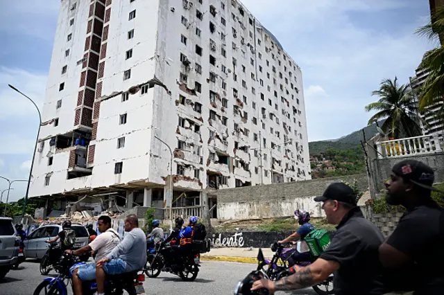 A large crack appears across a white tower block. The walls of one side of the building have crumbled and the paint has pealed away