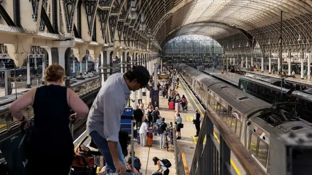 People at the top of steps with suitcases, below them are trains.