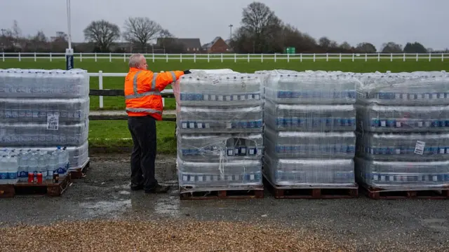 A man in an orange high vis jacket touching a crate of bottles of water.