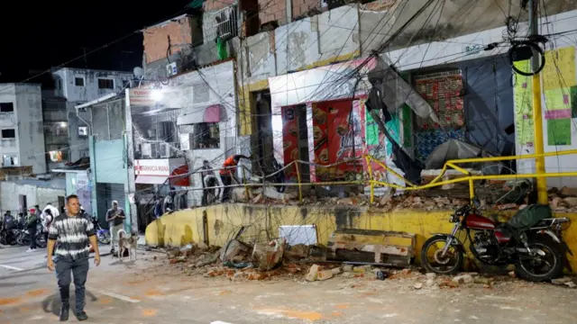 A man passes a street with damaged railings and shopfronts in the aftermath of an earthquake.