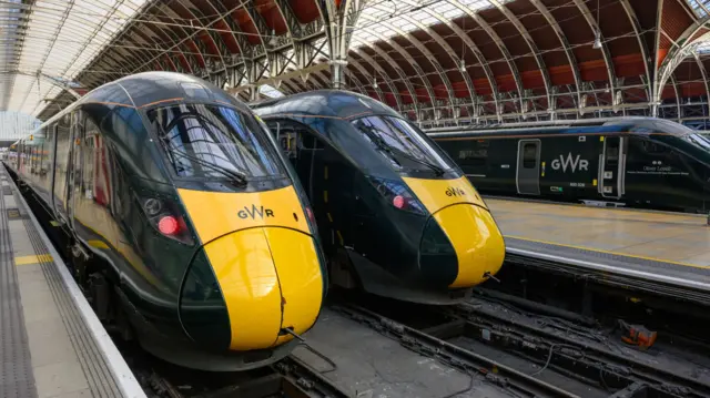 Three green and yellow GWR trains sit at a railway station.
