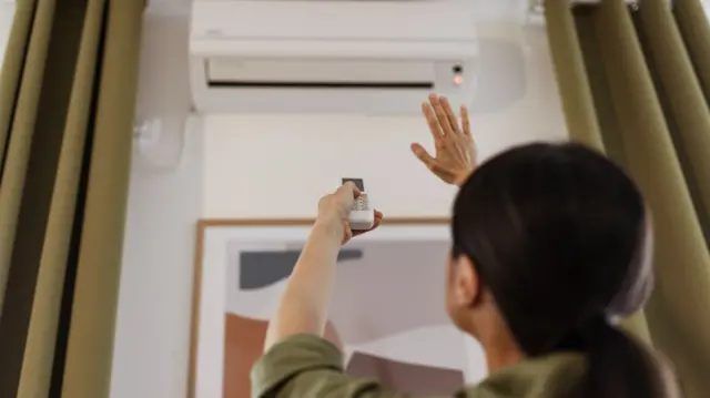 Woman holding remote control air-conditioner in house